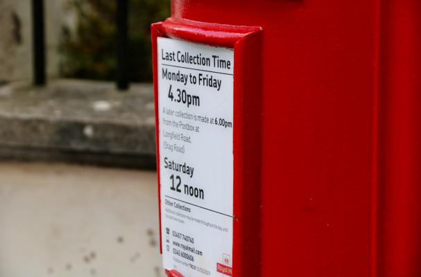 A bright red postbox on a street clearly displays its collection times
