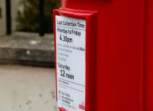 A bright red postbox on a street clearly displays its collection times